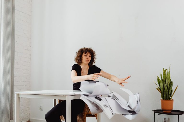 Woman frustrated and tossing paperwork at her office desk