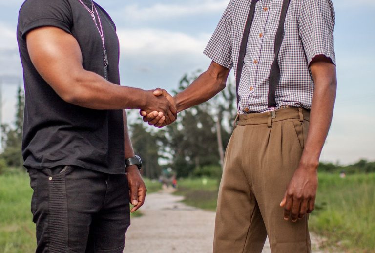 Two people shaking hands outdoors in a casual collaboration agreement