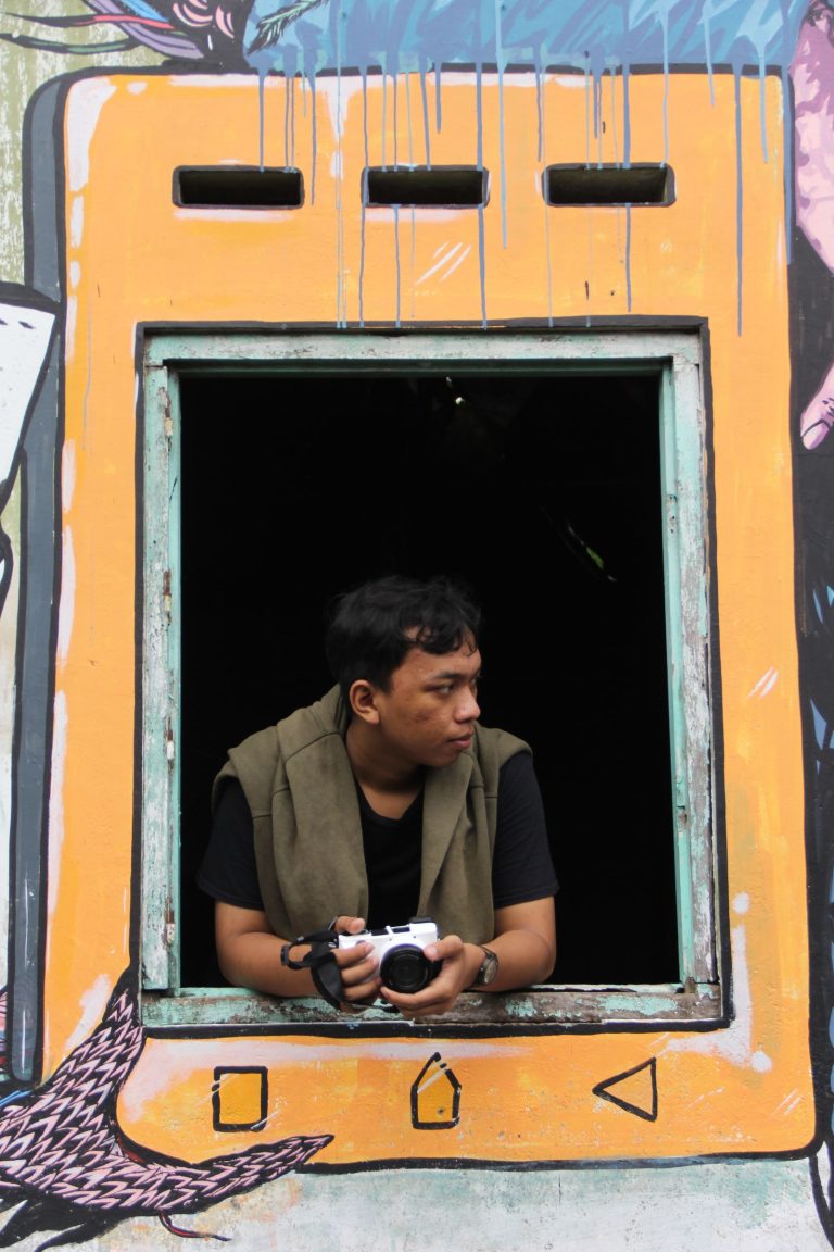 Man with a camera framed by a mural-decorated window in Bali